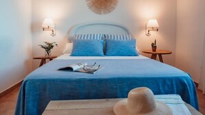 Un lit bien fait, avec une literie bleue, deux lampes de chevet, un objet décoratif fixé au mur et une petite table sur laquelle se trouvent un chapeau et un magazine.