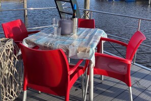 Una mesa con mantel de periódico, sillas rojas, una botella de vino y vasos sobre la cubierta de un barco.