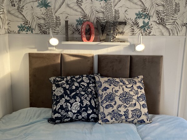 Una cama con cabecera, dos almohadones decorativos y una obra de arte en la pared.