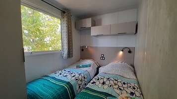 Una habitación pequeña y acogedora con dos camas, una ventana con cortinas y estanterías empotradas sobre las camas.