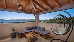 A covered outdoor seating area with a hanging chair, a cushioned bench, and a wooden table with fruit. - Villa San Zadarvillas (Sveti Filip i Jakov)