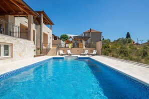 Una piscina con sillas de descanso, un muelle de madera y edificios de piedra.