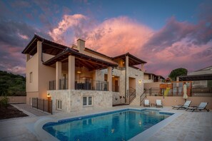Una casa moderna con piscina, mobiliario de exterior y zona de juegos infantiles.
