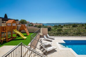 Zona de piscina con tobogán, tumbonas y vista al mar.