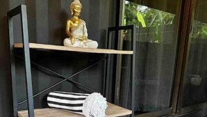 A black metal shelf with three wooden shelves, each with a white and black striped pillow. A golden Buddha statue is placed on the top shelf. - Villas Bodhi Soul Entero - Container Home and 2 Apartments - Saltwater Pool  (Savegre de Aguirre)