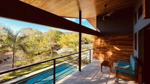 A modern outdoor pool area with a wooden ceiling, a view of a tropical landscape, and a seating area with blue cushions. - Villas Bodhi Soul Entero - Container Home and 2 Apartments - Saltwater Pool  (Savegre de Aguirre)