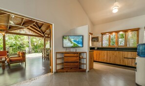 Een ruime woonkamer met een grote televisie, houten planken en uitzicht op weelderige begroeiing.