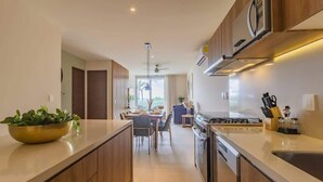 A modern kitchen with wooden cabinets, a central island, and a dining area with a view of the outdoors. - Ground-Floor Condo, Beach Club & 5 Rooftop Pools (Akumal)