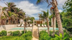 A pool area with lounge chairs, palm trees, and a pathway leading to a building. - Ground-Floor Condo, Beach Club & 5 Rooftop Pools (Akumal)