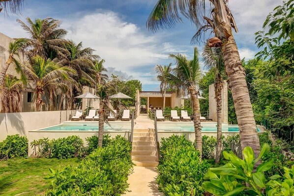 A pool area with lounge chairs, palm trees, and a pathway leading to a building.