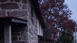 A stone building with a tiled roof, a pathway leading to a covered entrance, and a garden area with a lantern and a barrel. - Rustic Retreat country house (Tondela)