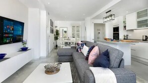 Una sala de estar moderna con un sofá gris, una mesa de centro blanca y un televisor de pantalla plana montado en la pared.
