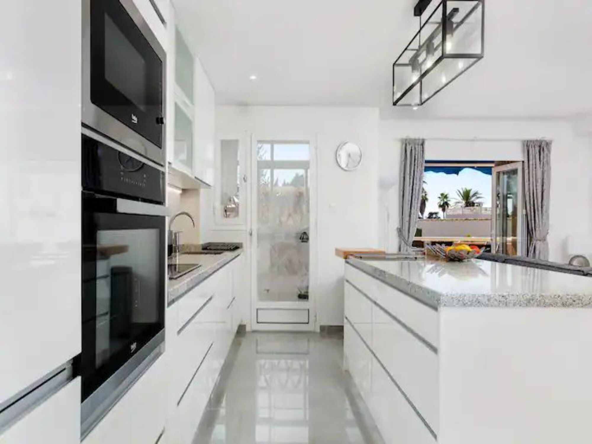 Une cuisine moderne avec des meubles blancs, un four en acier inoxydable et un grand îlot central doté d’un évier.