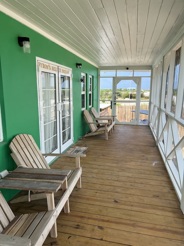 Eine überdachte Veranda mit Holzstühlen und einem Tisch, grünen Wänden und Blick auf den Strand.