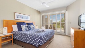 A bedroom with a bed, a nightstand, a dresser, a ceiling fan, and a window with blinds. - Resort on the Beach 5114 15 with resort Pool (Kingscliff)