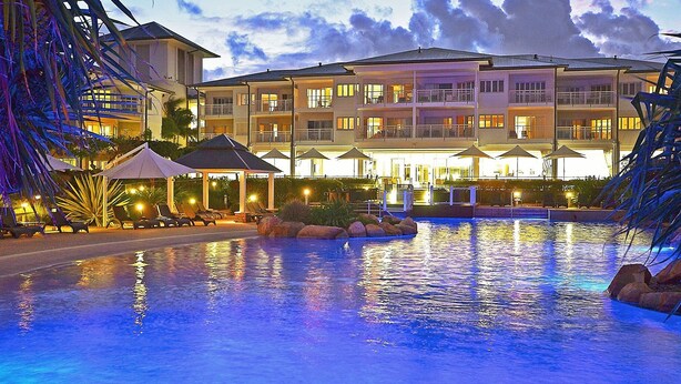 A hotel with a swimming pool, outdoor seating, and a well-lit facade. - Resort on the Beach 5114 15 with resort Pool (Kingscliff)