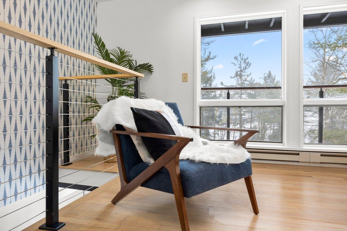 Una habitación moderna con un sillón azul, una manta suave de color blanco y un ventanal con vistas a árboles.
