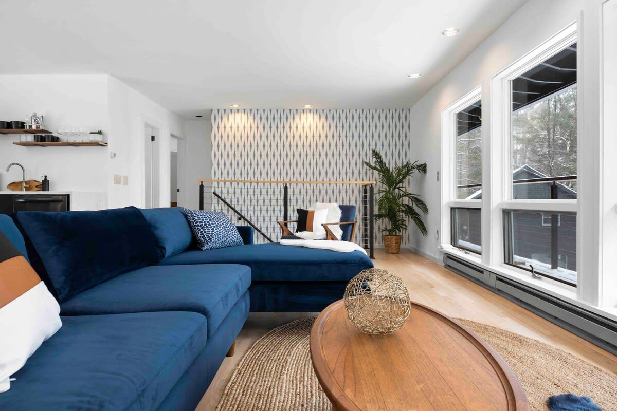 Una sala moderna con un sofá modular, una mesa de centro de madera y ventanas amplias.