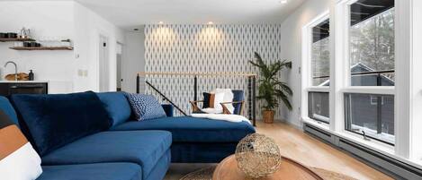 Una sala moderna con un sofá modular, una mesa de centro de madera y ventanas amplias.