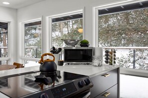 A modern kitchen with a large window, a kettle, a microwave, and a stove.