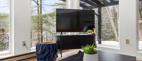A modern living room with a large flat-screen TV mounted on a black cabinet, a wooden coffee table with a remote control, and a potted plant.