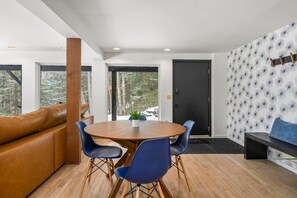 Un intérieur moderne avec une table ronde en bois, entourée de chaises bleues, d’un canapé en cuir marron et d’une porte noire.