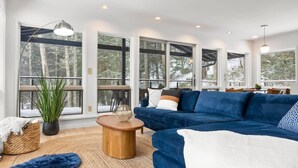 A modern living room with a blue sofa, a wooden coffee table, and large windows offering a view of trees. - Hudson Valley and The Berkshires getaway (Hillsdale)