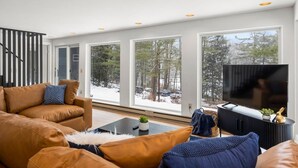 A modern living room with a large window, a sofa, a coffee table, and a TV. - Hudson Valley and The Berkshires getaway (Hillsdale)