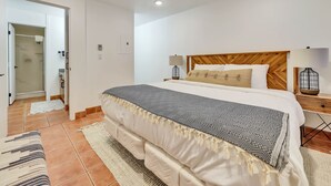 Een slaapkamer met een groot bed, twee bedlampen, een houten hoofdbord en een badkamer die door een open deur zichtbaar is.