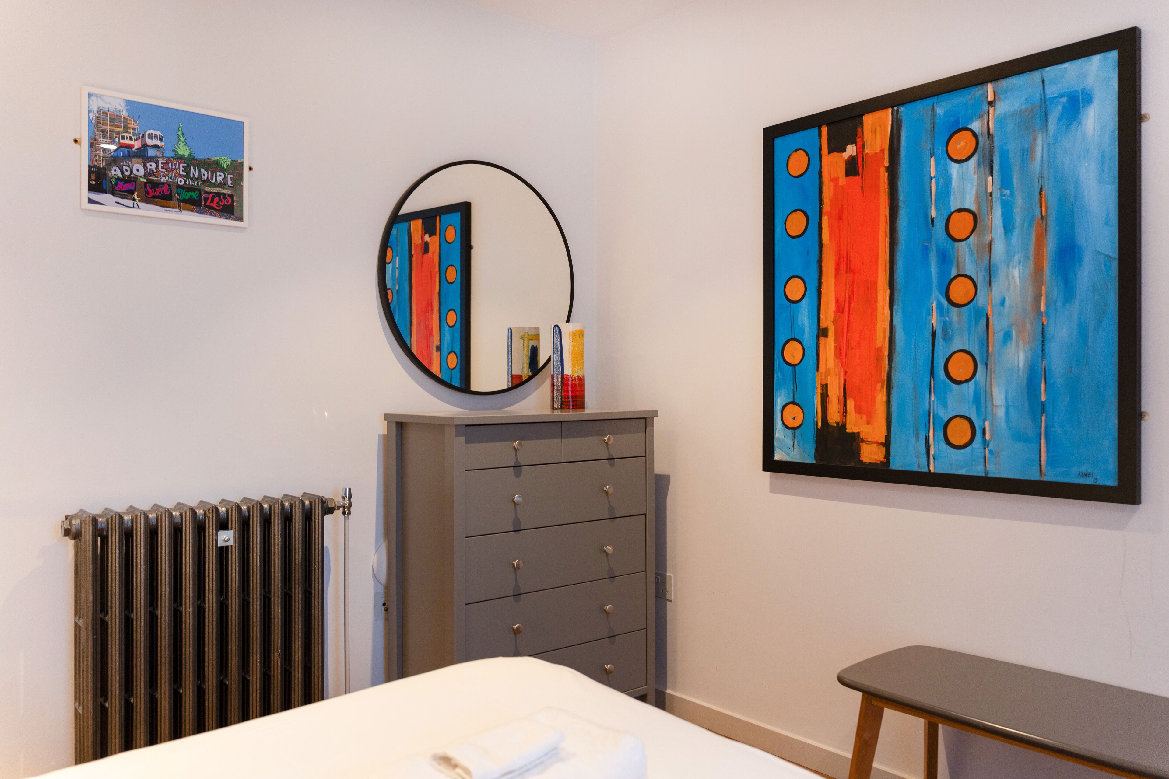 A bedroom with a bed, a dresser, a mirror, and a painting on the wall.