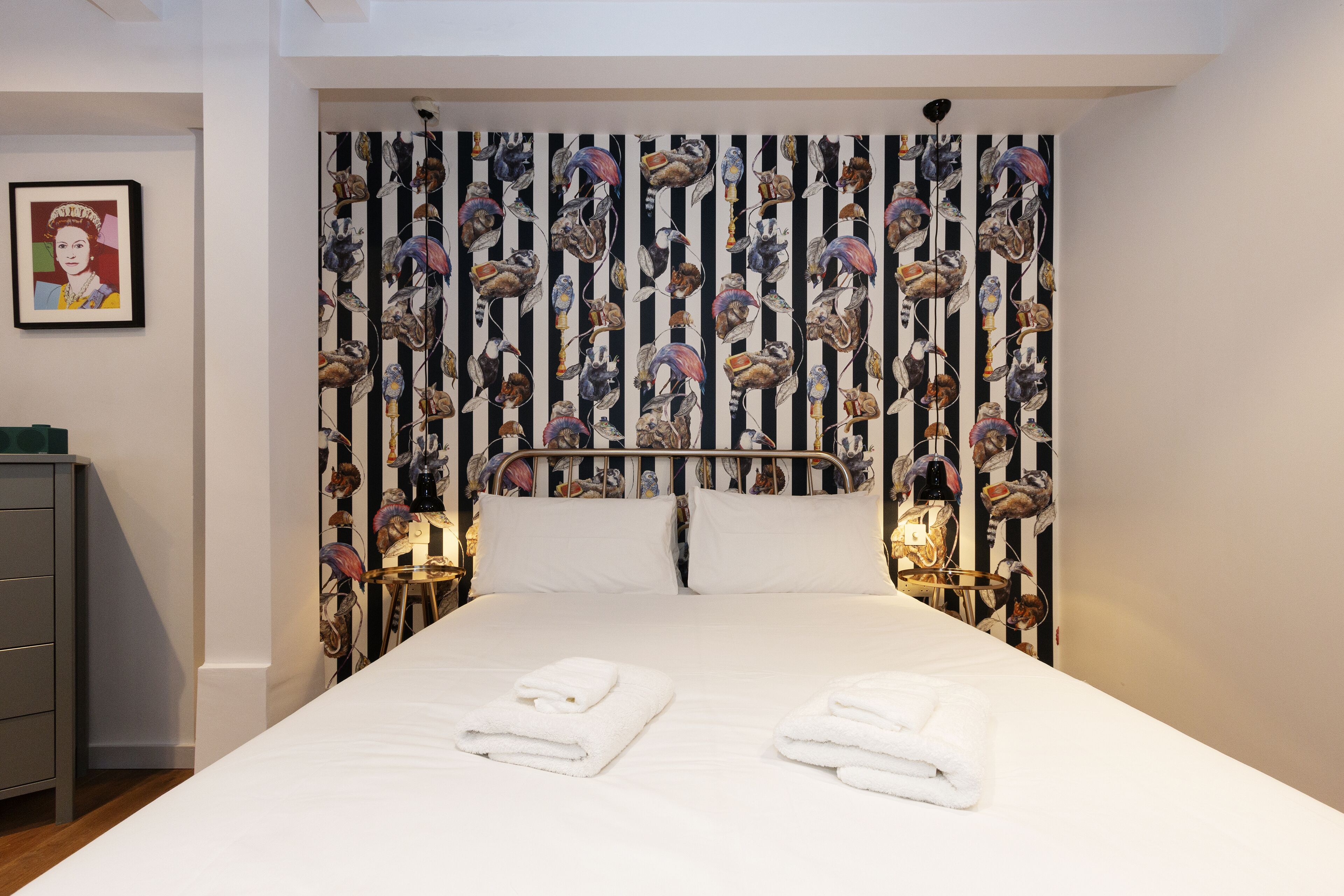 A neatly made bed with two folded white towels, a metal headboard, and a wall with a vertical striped pattern.