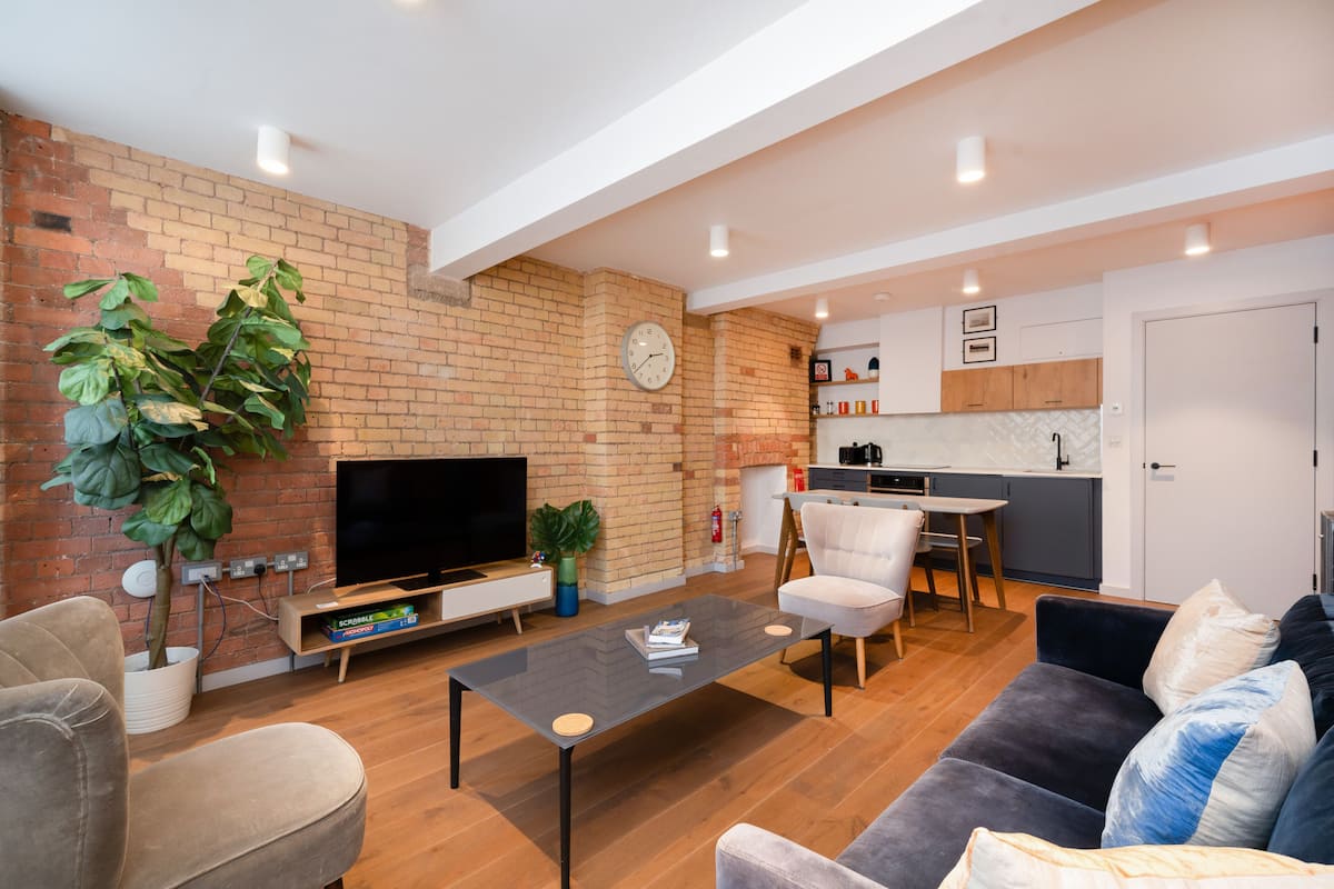 A modern living room with a brick wall, a flat-screen TV, a coffee table, and a sofa.