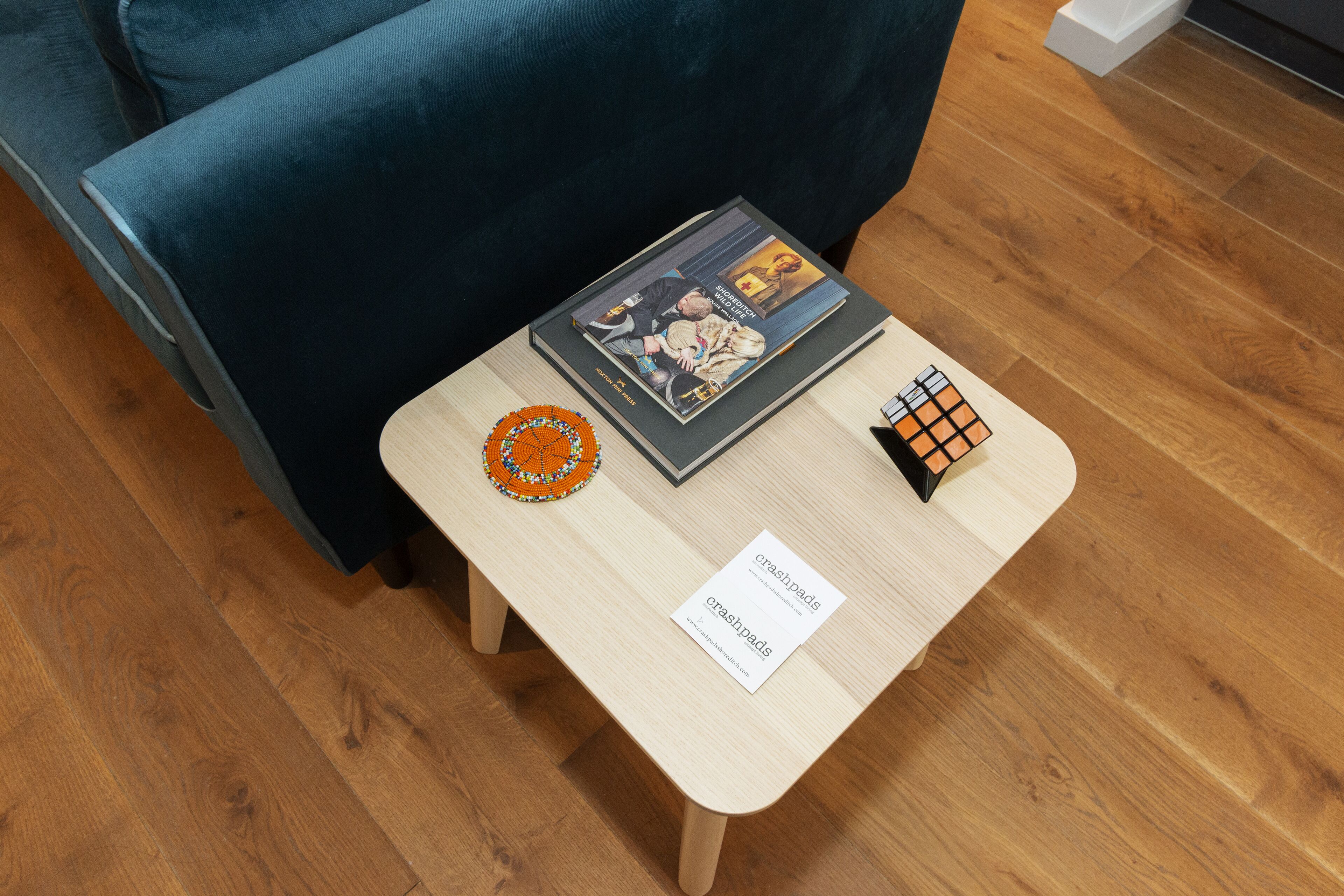 Een houten tafeltje met een tijdschrift, een klein oranje voorwerp en een witte kaart met tekst.