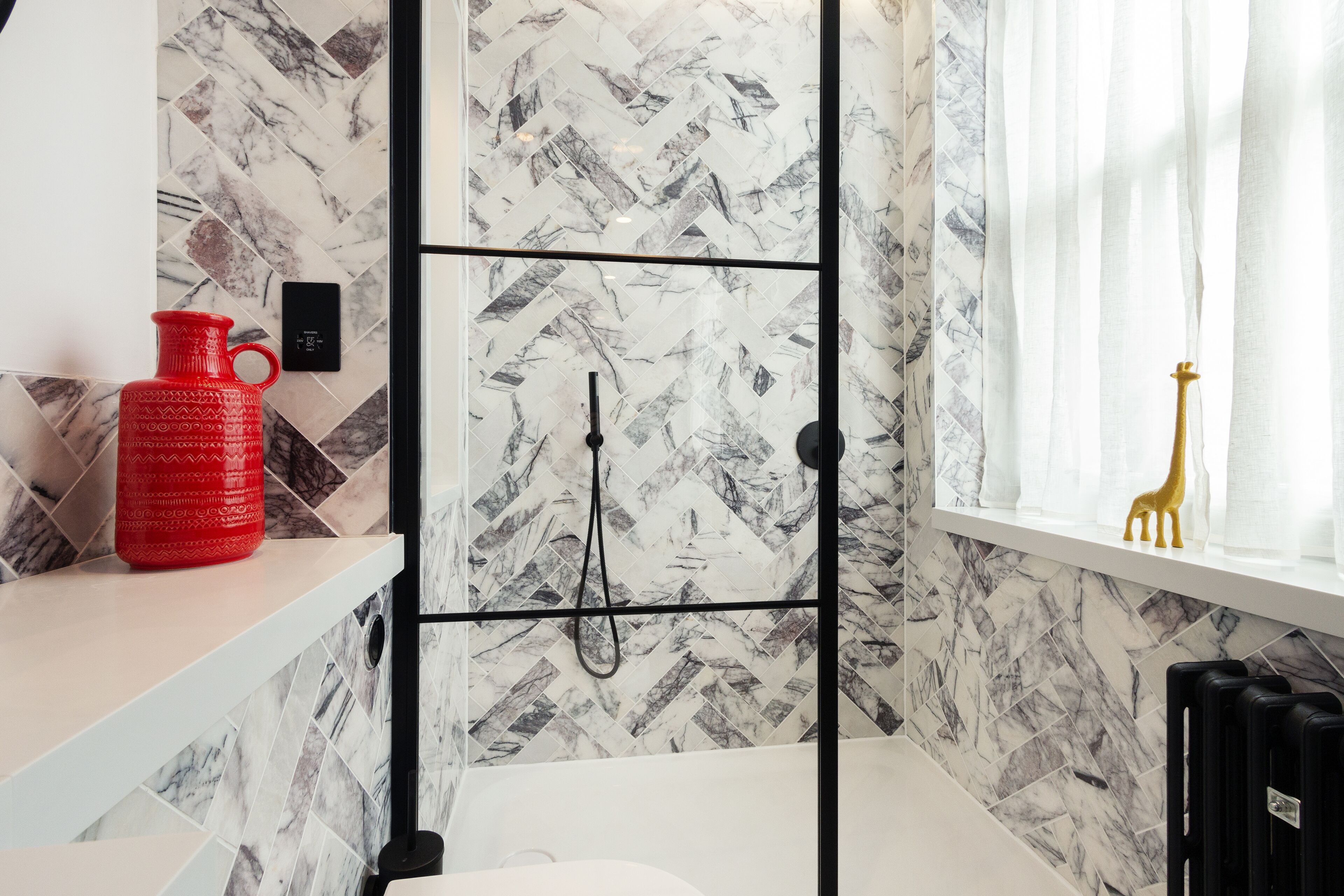 A bathroom with a shower, a red vase on a shelf, and a giraffe decoration on the window sill.