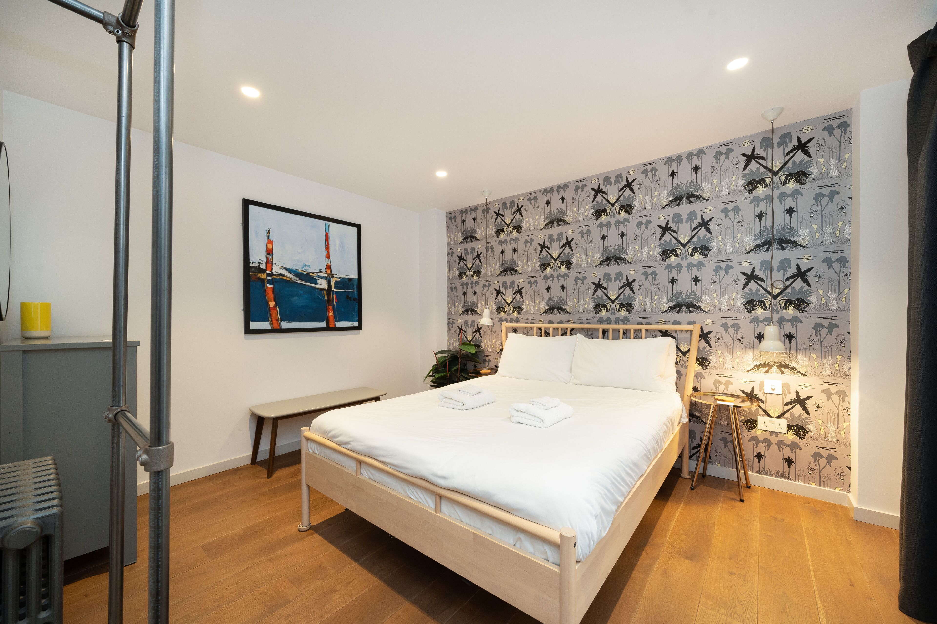 A bedroom with a bed, a bench, a desk, and a wall with a patterned wallpaper.