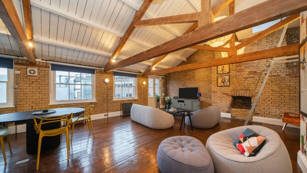 Un loft amplio con vigas de madera a la vista, pared de ladrillo, chimenea y un ventanal grande.