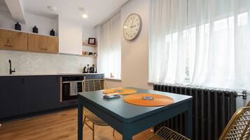 A modern kitchen with a blue table, wooden cabinets, and a clock on the wall.