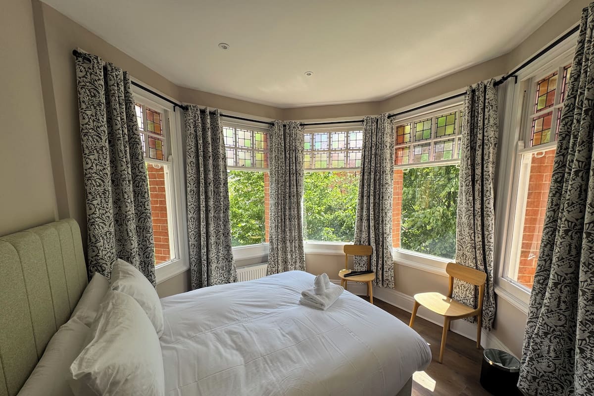 A bedroom with a bed, two chairs, and large windows with curtains.
