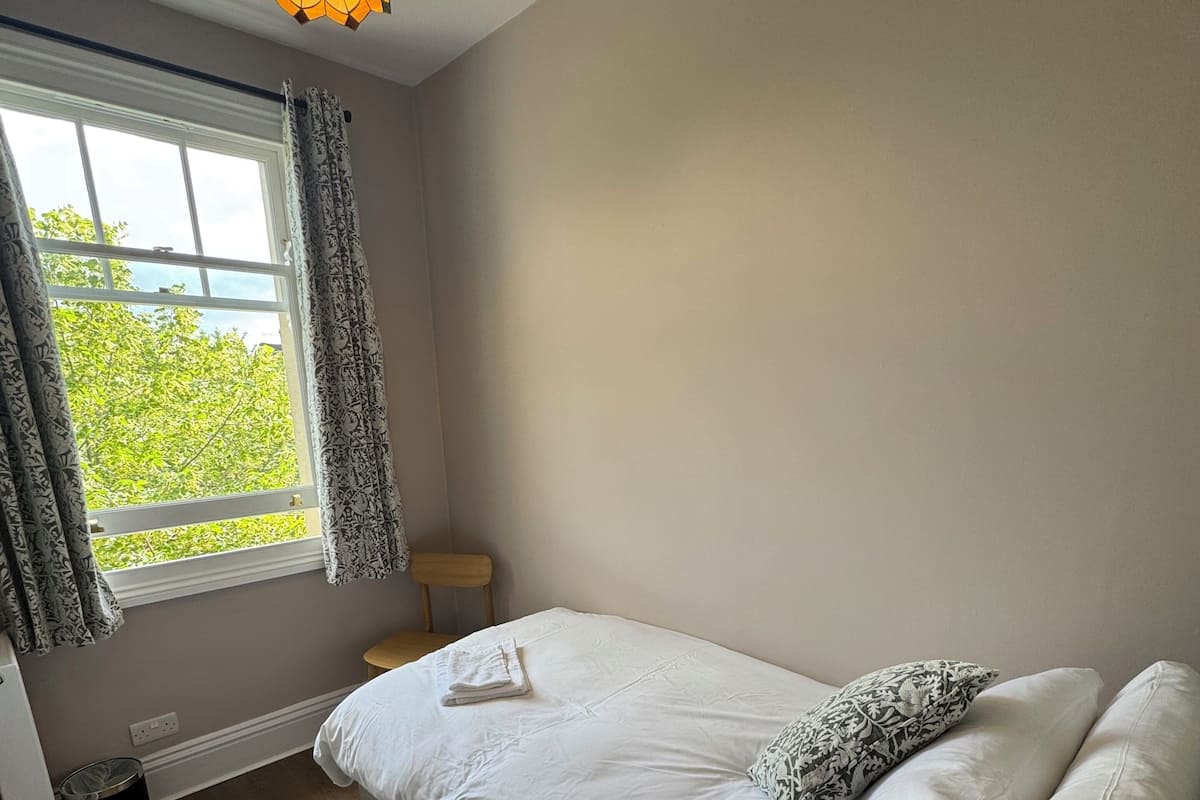 A bedroom with a bed, a window with curtains, a hanging light fixture, and a radiator.