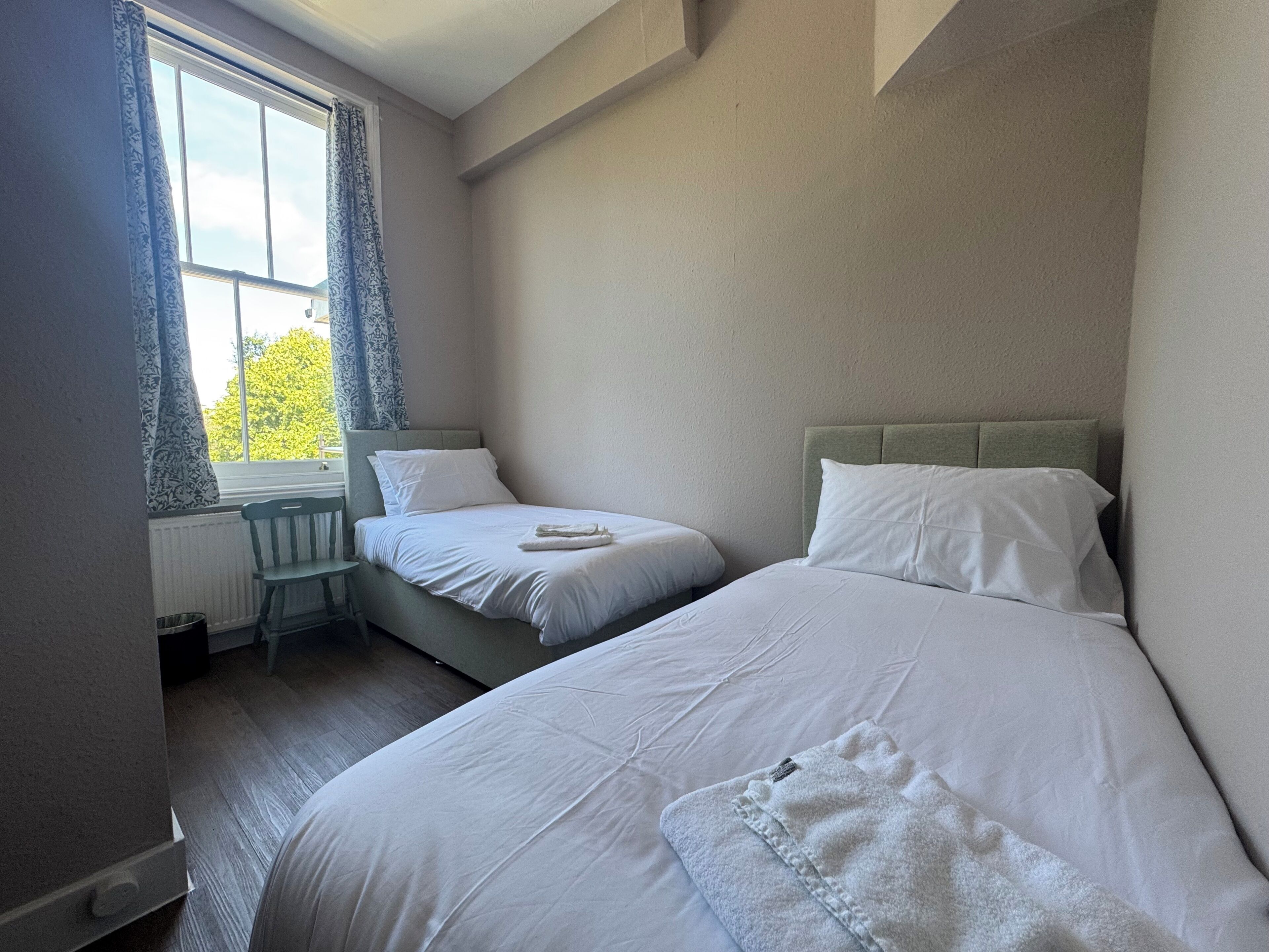 Un dormitorio con dos camas, una ventana con cortinas y un radiador.