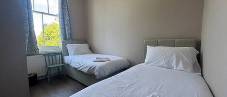 Un dormitorio con dos camas, una ventana con cortinas y un radiador.
