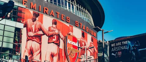 Estadio Emirates con un gran mural del equipo de fútbol Arsenal, asientos de estadio y un prominente logotipo de Arsenal.