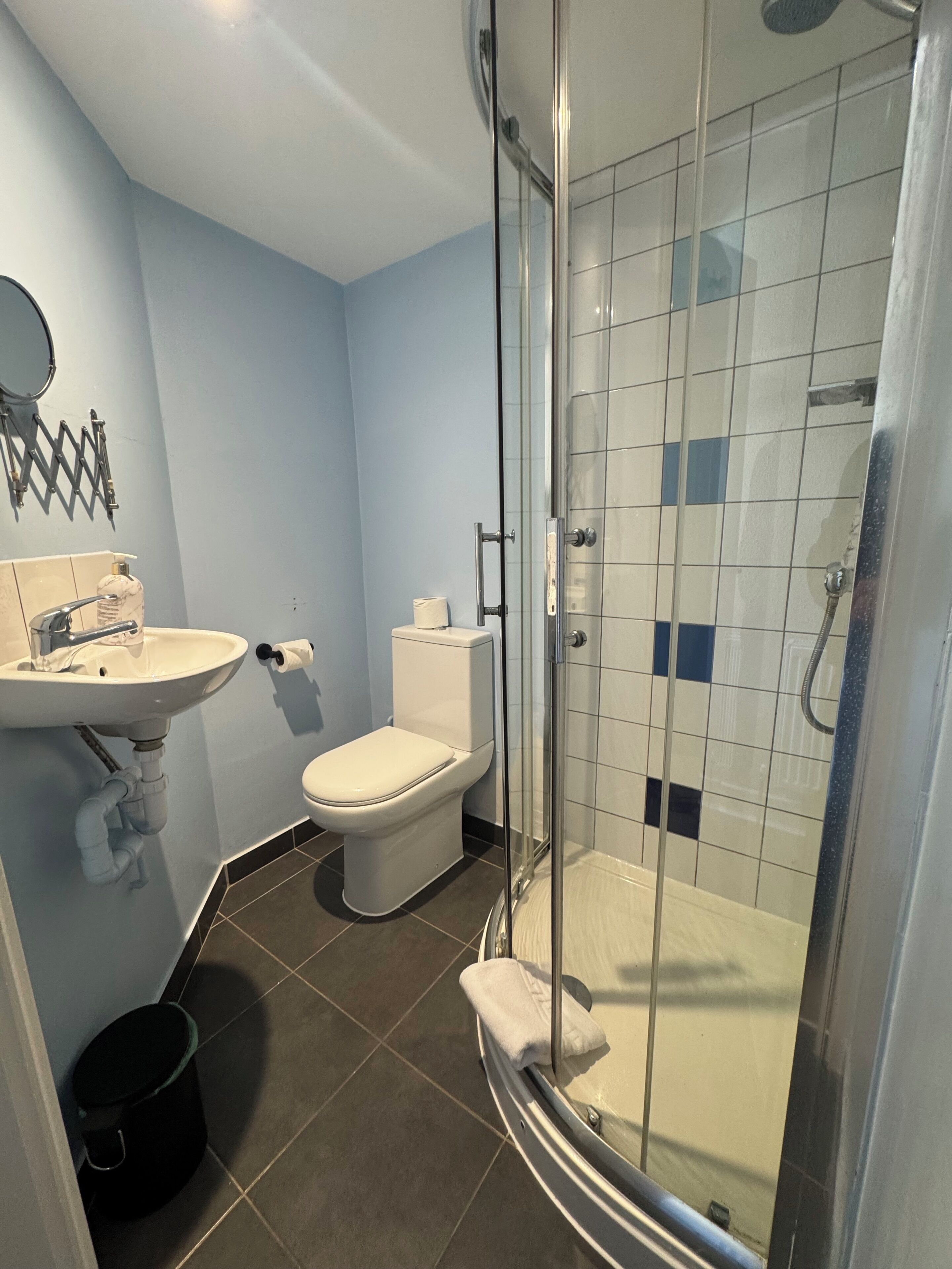 A bathroom with a glass-enclosed shower, a sink, a toilet, and a black trash bin.