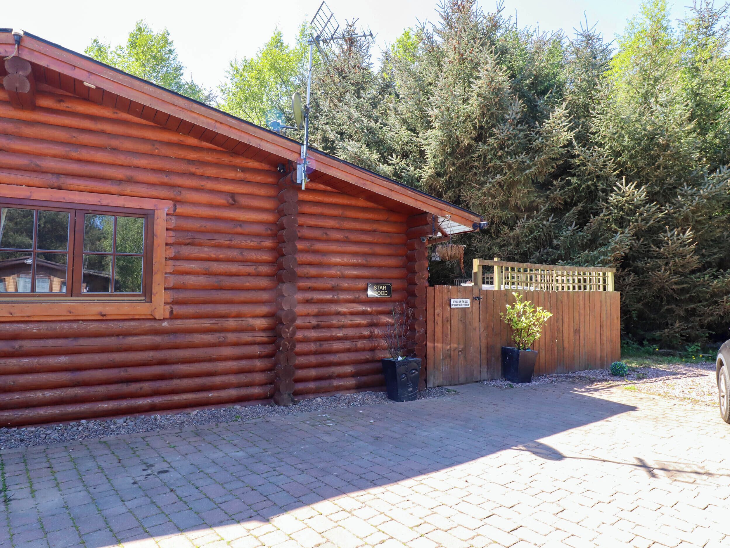 A wooden cabin with a window and a door, surrounded by trees and a wooden fence.