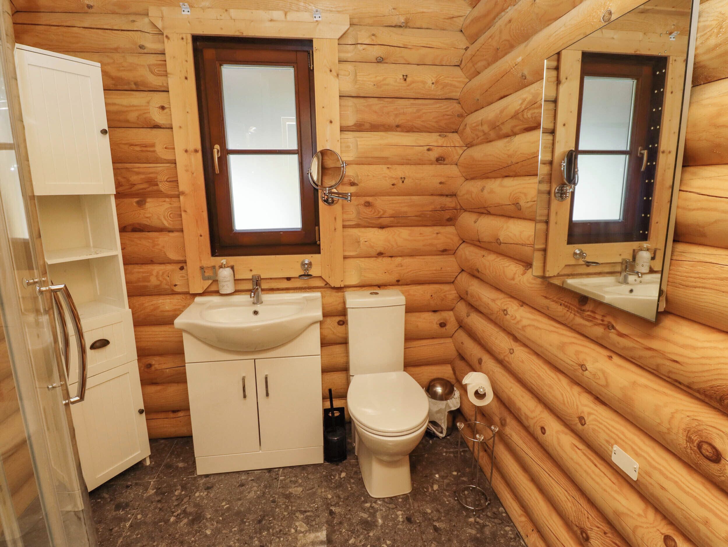 A compact wooden cabin bathroom with a sink, toilet, and a mirror above the sink.