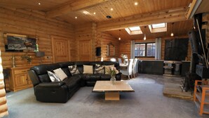 Interno di una baita di legno con un divano a pantaloncini in pelle nera, un tavolino in legno e un'area pranzo con tavolo e sedie.