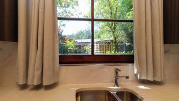 Un baño con lavamanos, una ventana con cortinas y vistas a árboles y un edificio.