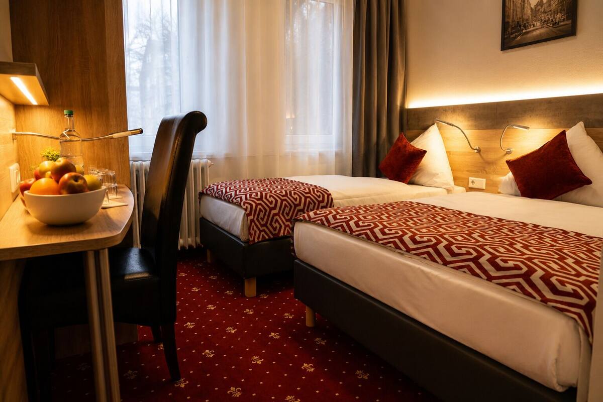 Ein Hotelzimmer mit zwei Betten, einem Schreibtisch mit Obstschale, einem Stuhl und einem Fenster mit Vorhängen.