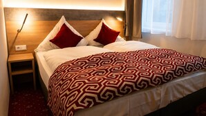 Habitació d'hotel amb un llit, dos coixins, una taula de nit, una làmpada i una finestra amb cortines.