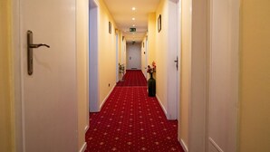 Passadís d'hotel amb una catifa vermella, parets blanques i portes a banda i banda.